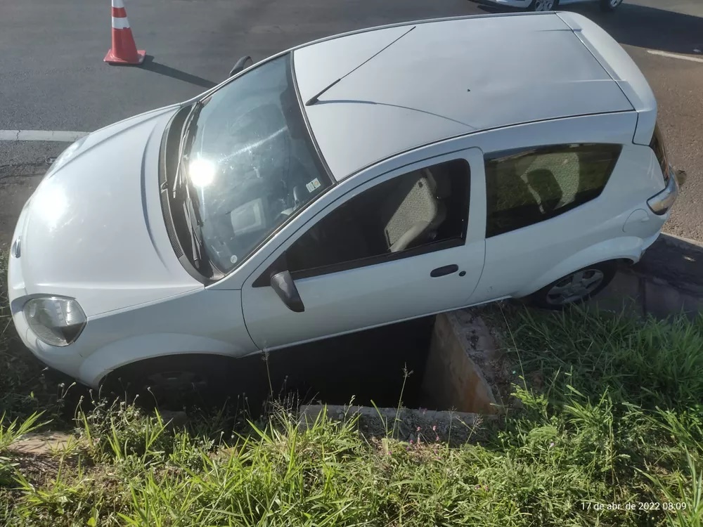 Carro fica enroscado em bueiro de rotatória após motorista perder o controle da direção